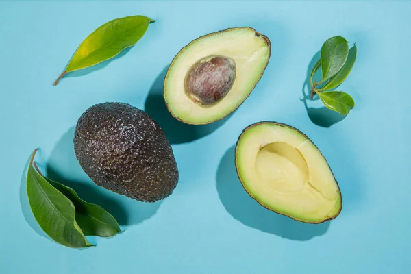 Skivor av avokado på ljus bakgrund. Hela och halva med blad. Designelement för produktetikett — Stockfoto