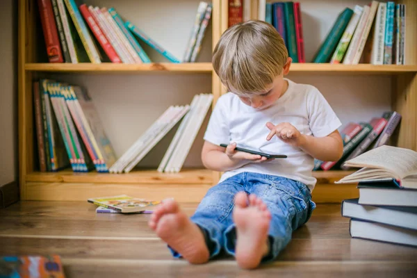 Çocuk kitap rafları önünde onun smartphone ile oynamak — Stok fotoğraf
