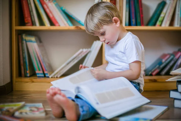 Çocuk kitap rafları önünde büyük bir kitap okuma — Stok fotoğraf