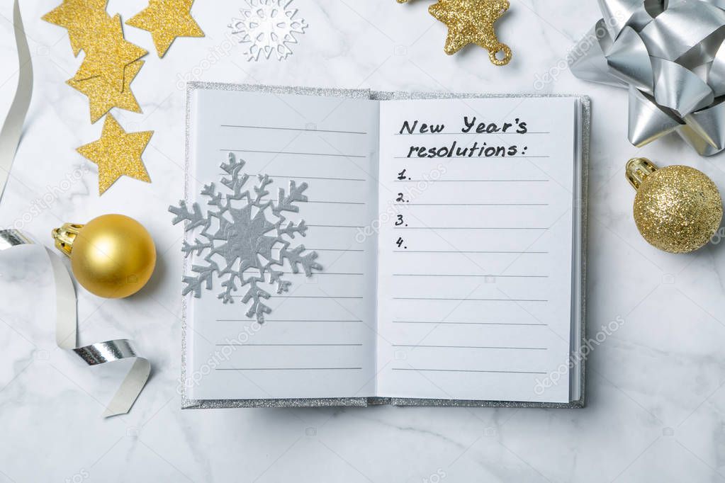 New year resolutions concept - notebook with list of goals and silver gold decorations