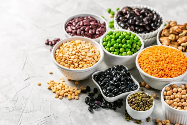 Selection of legumes in white bowls on stone background — Stock Photo, Image