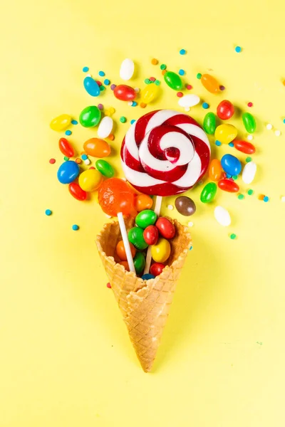 Pirulopops e doces em cone de sorvete em fundo amarelo brilhante — Fotografia de Stock