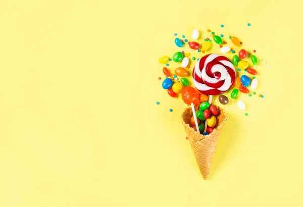 明亮的黄色背景冰淇淋蛋筒中的棒棒糖和糖果 — 图库照片