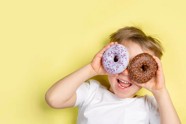 Niño sosteniendo donuts por este ojos, fondo brillante —  Fotos de Stock