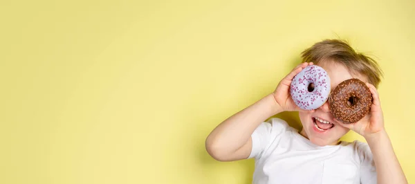 Niño sosteniendo donuts por este ojos, fondo brillante —  Fotos de Stock