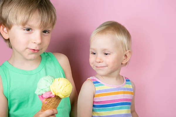 快乐的男孩和女孩吃冰淇淋在粉红色的巴克地面前 — 图库照片