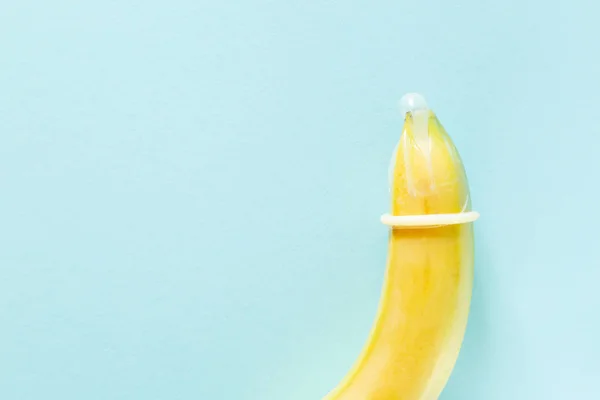 Sex education concept - banana in condom on pastel background — Stock Photo, Image