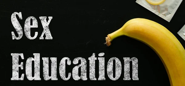 Sex education concept - letters, banana and condoms on blackboard — Stock Photo, Image