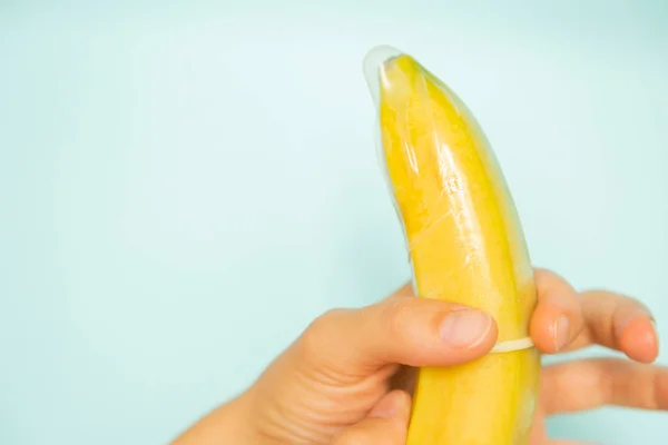 Sex education concept - hands putting condom on banana pastel background — Stock Photo, Image