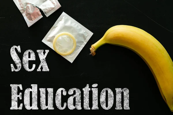Sex education concept - letters, banana and condoms on blackboard — Stock Photo, Image