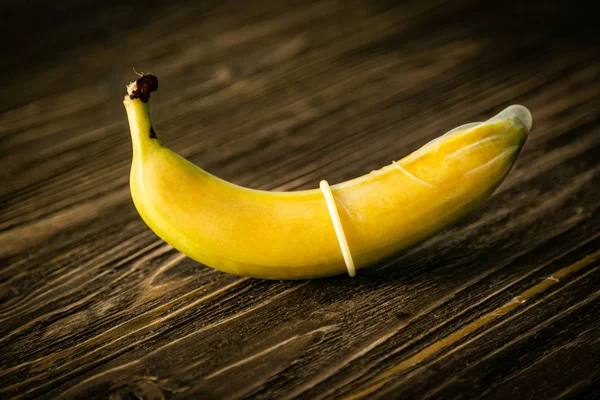 Sex education concept - banana in condom on wood background — Stock Photo, Image