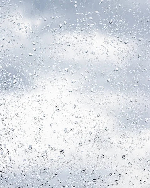 Rain drops on window glasses surface with cloudy sky background . Natural backdrop of raindrops. Abstract overlay for design. The concept of bad rainy weather.