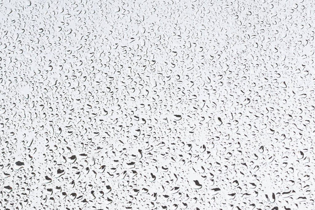 Rain drops on window glasses surface with gray sky background . Natural backdrop of raindrops. Abstract overlay for design. The concept of bad rainy weather.