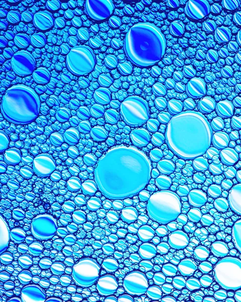 Top view on colorful drops of oil on the water. Blue circles and ovals. Abstract bright background for design with reflection.