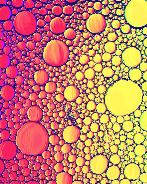 Top view on a colorful drops of oil on the water. Rainbow or spectrum colored circles, ovals. Abstract bright background for design with reflection and refraction.