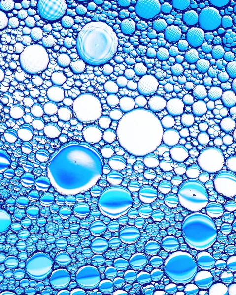 Top view on colorful drops of oil on the water. Blue circles and ovals. Abstract bright background for design with reflection.