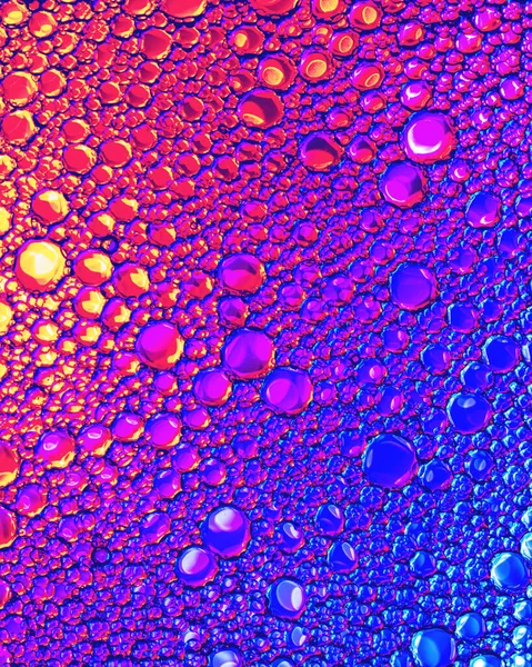 Top view on a colorful drops of oil on the water. Rainbow or spectrum colored circles, ovals. Abstract bright background for design with reflection and refraction.