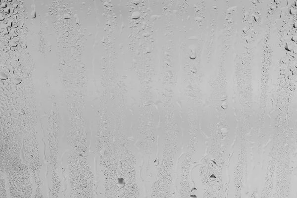 Rain drops on window glasses surface with gray sky background . Natural backdrop of raindrops. Abstract overlay for design. The concept of bad rainy weather.
