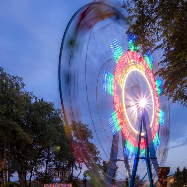 Rotating Ferris wheel in a night park with neon lighting against the sky.
