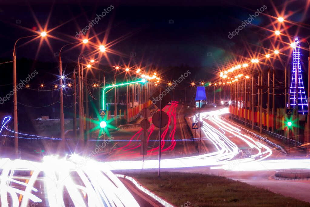 Traces of headlights from cars moving at night on the bridge, illuminated by lanterns. Abstract city landscape with highway at dusk. 
