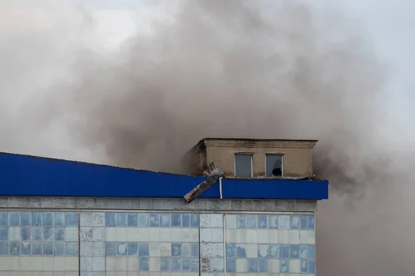 Black smoke rising from a burning building with a cloudy sky in the background.