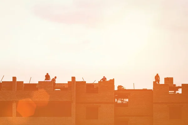 Silhouette of a team of construction workers constructing a building against the background of a sunset sky in the evening.
