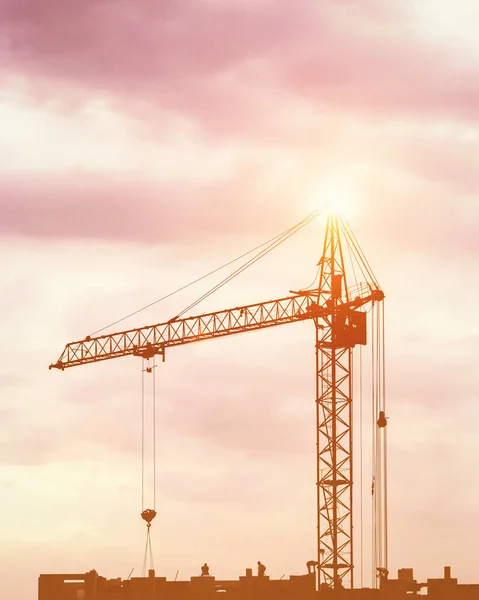 Silhouette of a team of construction workers in and a crane constructing a building on the background of the evening sunset sky.