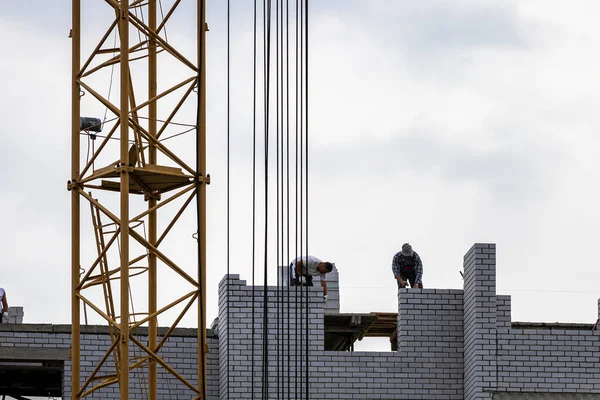 A team of construction workers in and a crane constructing a building on the background of the evening cloudy sky.