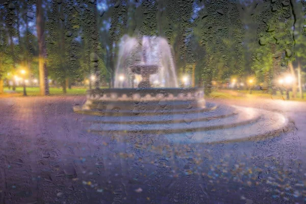 Fuente Desenfocada Parque Nocturno Con Luces Detrás Vidrio Húmedo Lluvioso — Foto de Stock