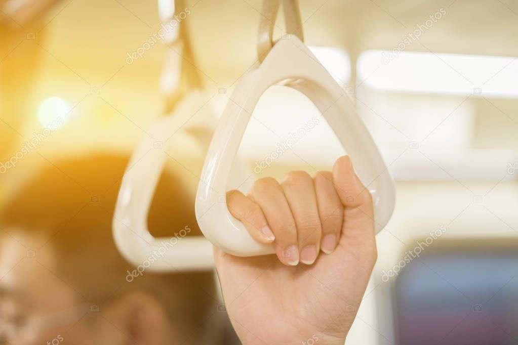 female hand holding white handles hanging on ceiling of bus 