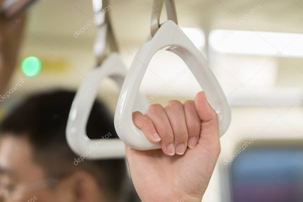 female hand holding white handles hanging on ceiling of bus 