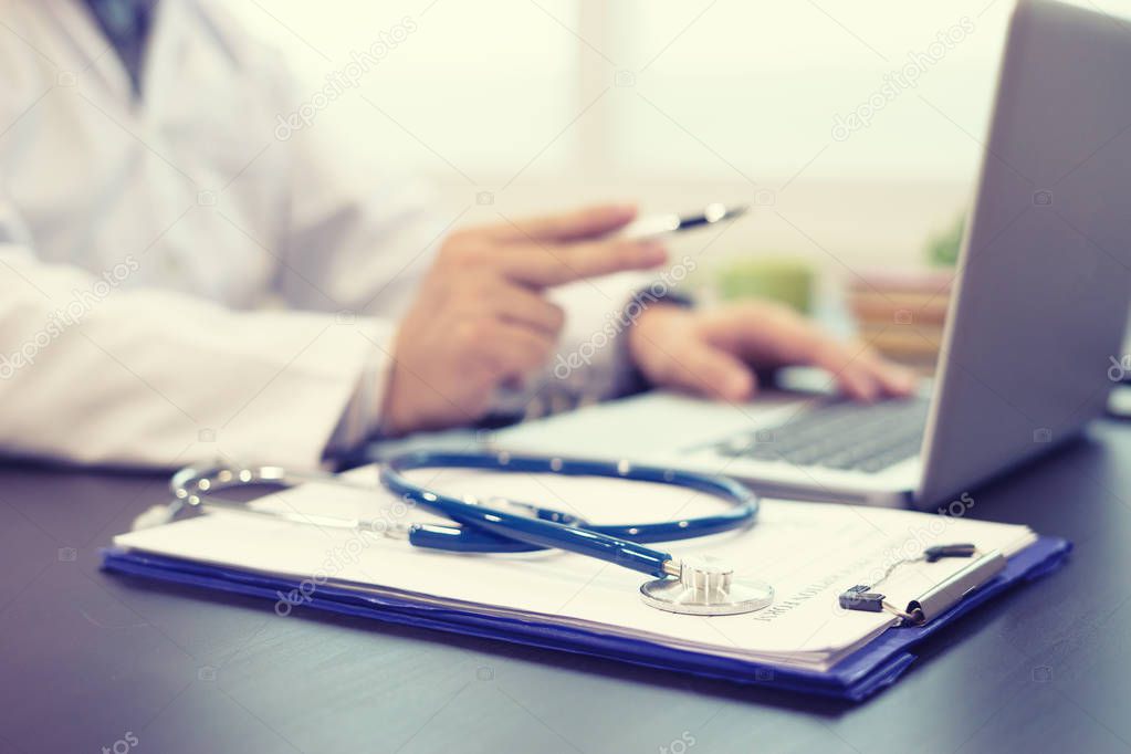 Doctor writing prescription and using laptop in hospital