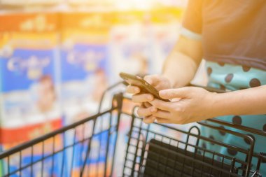 Süpermarkette arabası üzerinde Smartphone elle tutan kadın