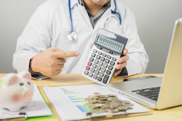 male doctor counting money on calculator and working with laptop in office