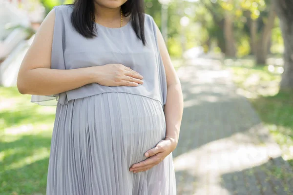 happy pregnant woman touching belly outdoors in park