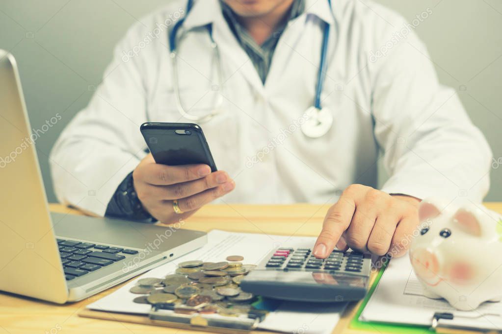 Doctor holding smartphone and counting coins with calculator