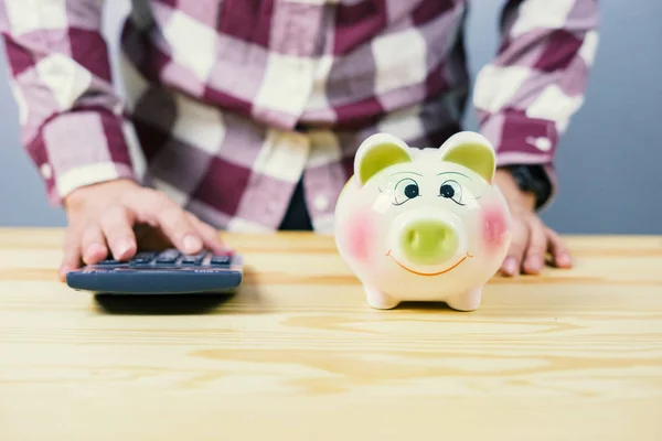 cropped image of man using calculator at home, piggy bank on table