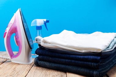 iron and stack of jeans and t-shirt clothes on wooden plank,blue background clipart