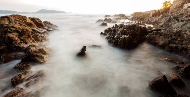 Uzun pozlama görüntü günbatımı manzara arka planda rock ile dramatik gökyüzü ve dalga deniz manzarası
