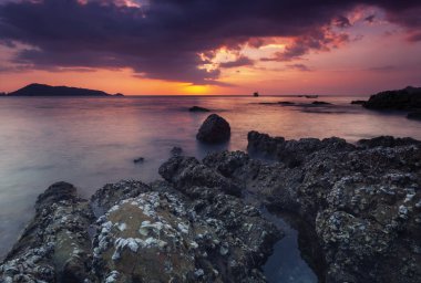 Uzun pozlama görüntü günbatımı manzara arka planda rock ile dramatik gökyüzü ve dalga deniz manzarası.