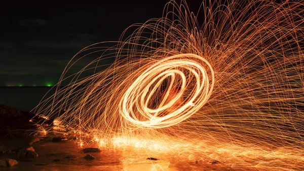 Swing fire Swirl steel wool light photography over the stone with reflex in the water long exposure speed motion style.
