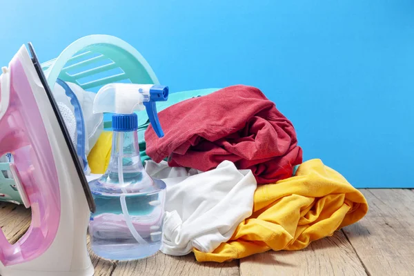 Pile of colorful clothes and irons,spray bottle on wooden plank ,blue color background.