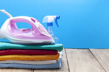 Renkli elbise ve ütüler, ahşap tahta, mavi renk arka plan üzerinde sprey şişe yığını.