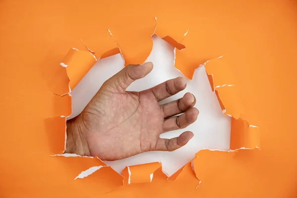 Мужская рука разорвал оранжевую бумагу на белом фоне — стоковое фото