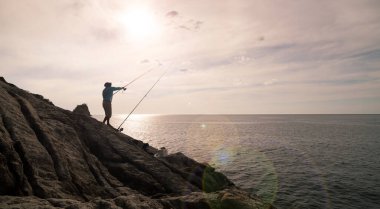Kayalıklarda balık tutan genç bir adamın silueti. Tayland 'da mercekli olta kamışı tutuyor.