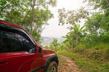 Kırmızı SUV yaz arabası ve dağlarda yol ormanda toprak yolda süsleme için boş alan yeşil orman arka planda kırsal bölge macerası