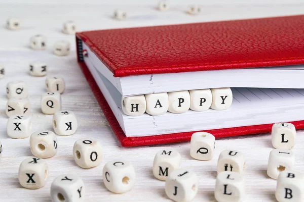 Word Happy written in wooden blocks in red notebook on white wooden table. Wooden abc.