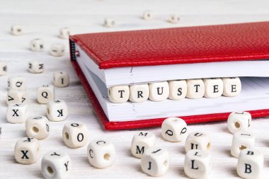 Word Trustee written in wooden blocks in red notebook on white wooden table. Wooden abc. clipart
