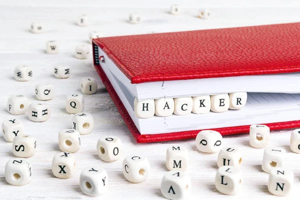 Word Hacker written in wooden blocks in red notebook on white wooden table. Wooden abc.