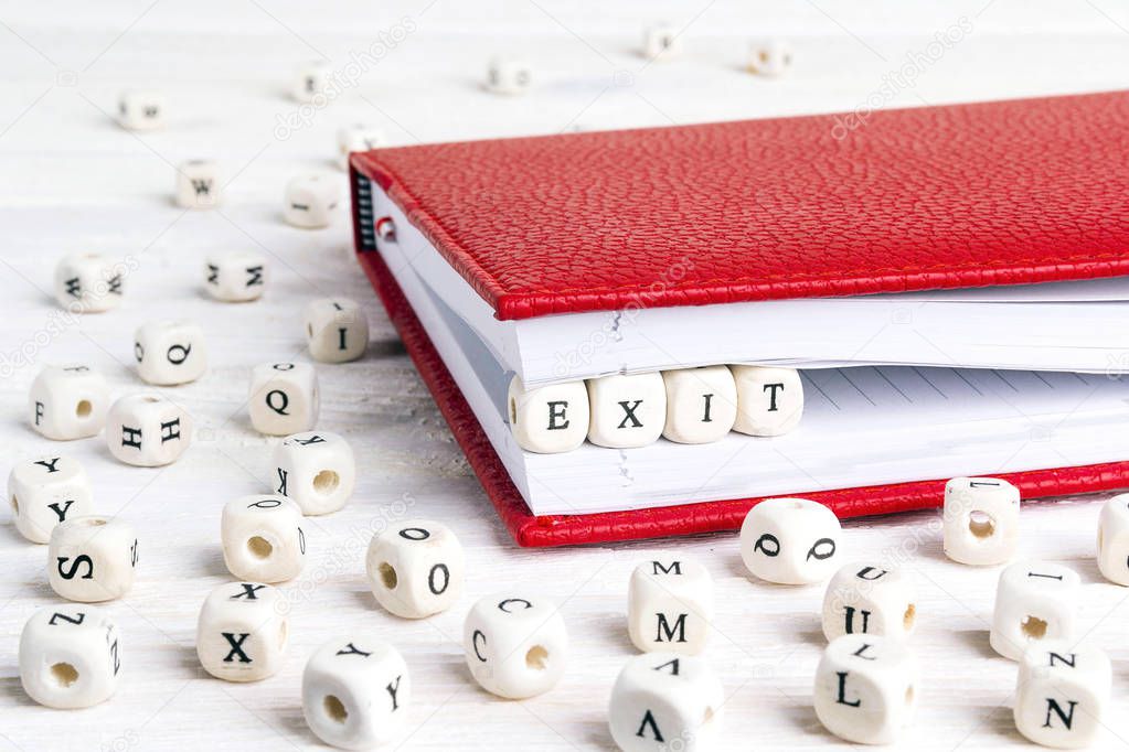 Word Exit written in wooden blocks in red notebook on white wooden table. Wooden abc.
